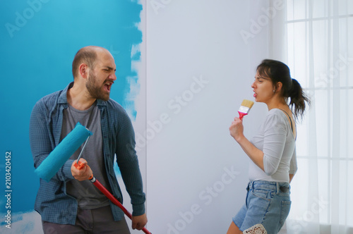 Bild auf Leinwand Happy young family singing on roller brush while giving their apartment a makeover, apartment redecoration and home construction while renovating and improving