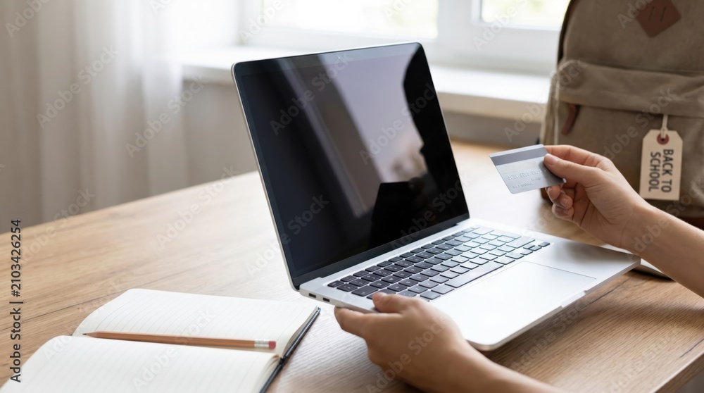 Fototapeta premium Young female student shopping online for school supplies using a credit card and laptop at home desk, preparing for back to school season with digital payment technology