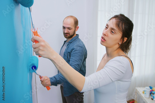Foto Girlfriend and boyfriend painting wall with blue paint during living room makeover, apartment redecoration and home construction while renovating and improving