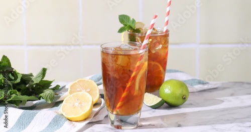Woman stirring refreshing ice tea with citrus fruits in glass at light marble table indoors, closeup