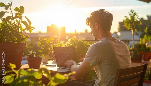 Young man working on laptop at sunset on rooftop balcony with potted plants, remote work lifestyle, digital nomad productivity