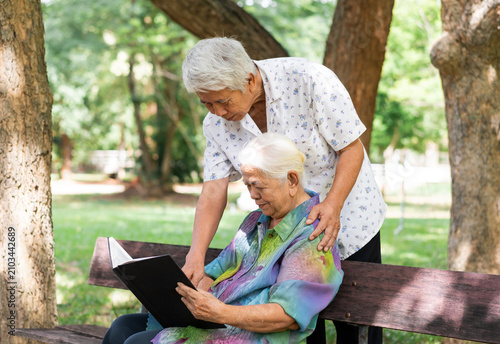 Obraz na płótnie Happy Asian senior couple reading book together on bench in green park