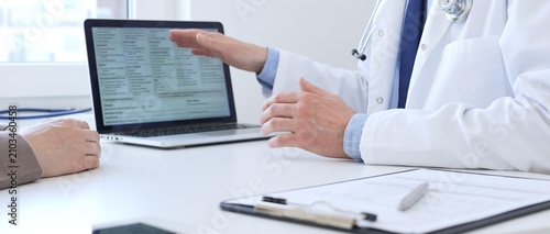 Close-up of a doctor reviewing digital test results with patient, discussing health findings on laptop screen during clinical consultation. Medicine and health care concept
