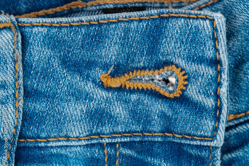 Картината върху платно Closeup of blue denim fabric featuring buttonhole with frayed edges contrasting orange stitching