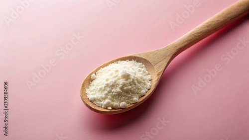 A delicate dusting of colostrum skim milk powder coated a vintage wooden spoon on a soft pink background