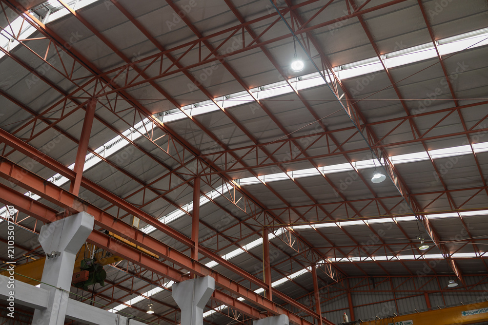 Obraz premium Vast impressive interior roof structure of an industrial factory concept featuring sturdy steel beam frame and corrugated metal sheet roofing with bright skylight illumination