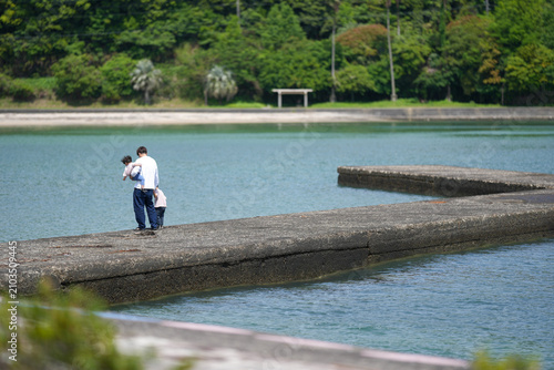 Foto Man holds child on rocky jetty near calm water