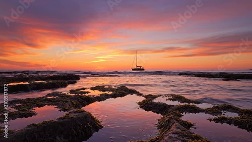 A lonely sailboat drifts on the calm ocean during a vibrant sunset