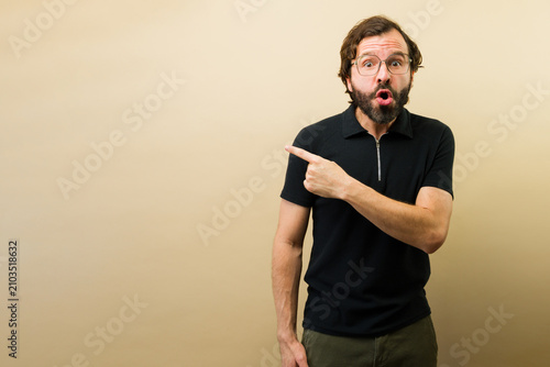 Fotografía Surprised man pointing to the side, open mouth showing reaction