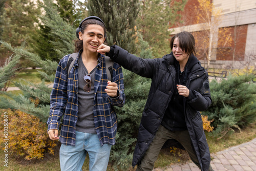 фотографія A young woman playfully punches her male friend on the chin while both are laughing and enjoying student life outdoors
