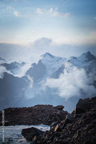 Mystical morning view of the mountain range with mist and clouds covering the sharp peaks of Tian Shan.