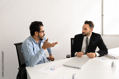 фотографія Two multiethnic businessmen, male colleagues discussing financial report, developing marketing strategy at meeting in corporate office