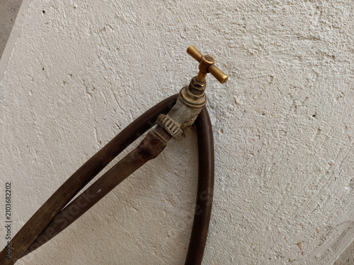 Obraz na płótnie Old brass tap on a white concrete wall connected to pipe hose