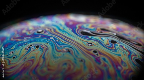 Macro photography of a soap film texture showing vibrant rainbow iridescence and fluid swirl patterns