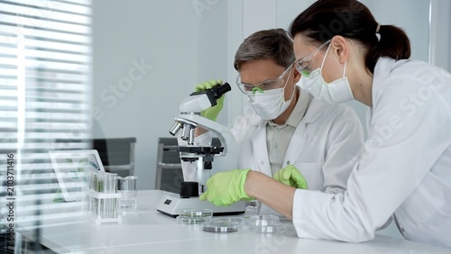 Scientists wearing lab coats. Safety glasses. Masks. And gloves working together in a contemporary laboratory