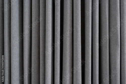 Grey textured fabric curtain background with deep vertical folds.