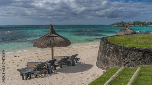 Schilderij op canvas A row of sun loungers under a straw umbrella on a sandy beach