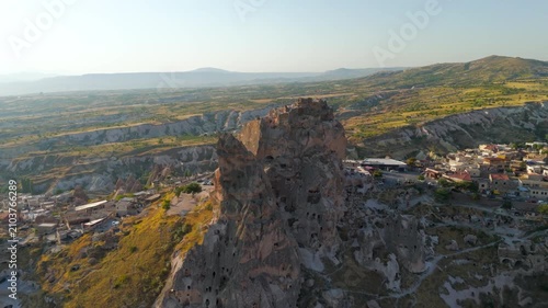 Uchisar, Nevsehir, Turkey. Uchisar Castle, a massive volcanic tuff rock formation carved with tunnels and chambers, aerial view over Cappadocia at golden hour. Aerial View, Departure of the camera