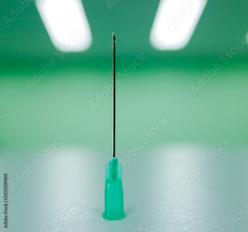 Fotografie Sterile medical hypodermic syringe needle standing vertically on green backgr