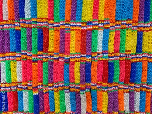 Colorful floral pattern background made from vibrant artificial flower garlands in a traditional Thai style. Bright multicolor decorative texture with geometric striped design.