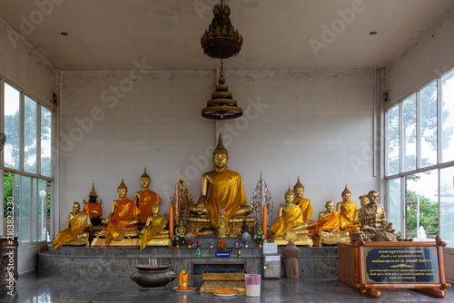 Photos Golden Buddha statues arranged on a raised altar inside a brightly lit temple shrine with incense burners