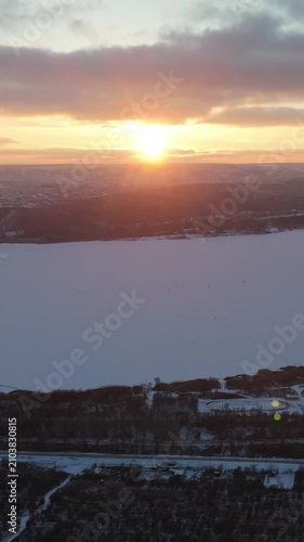 Sunrise over frozen lake with snow-covered landscape and distant hills, showcasing the gradual illumination of the horizon and the serene winter atmosphere