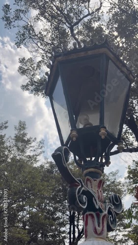 Close-up video footage of a vintage decorative street lamp surrounded by green trees in a public park. Classic architectural design combined with natural surroundings creates an elegant outdoor