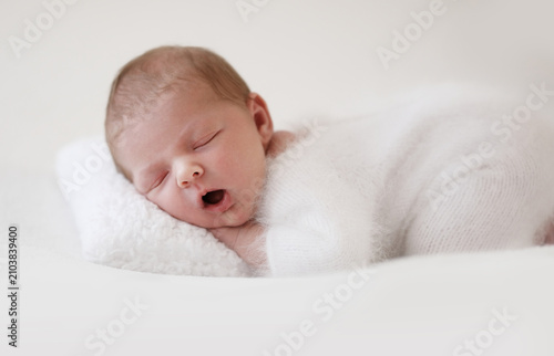 Cuadro en lienzo Newborn Sleeps Quietly On Fluffy White Pillow Wearing Cozy White Outfit And Hat With Hands Tucked Under Chin