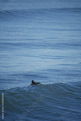 surfer paddling through cold water in winter Aotearoa New Zealand, Pacific waves New Brighton beach in Christchurch, Aotearoa New Zealand