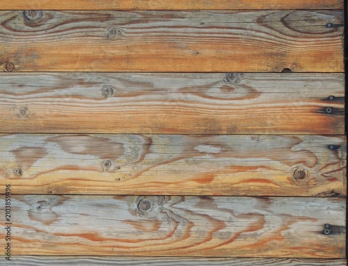 An old wall made of horizontal wooden planks. The surface has a contrasting natural grain pattern with transitions from red to gray, with pronounced knots and old nail heads.