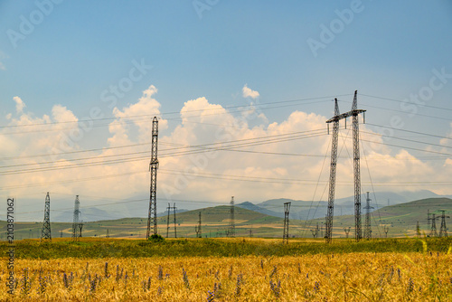 Quadro su tela Power transmission towers line open countryside under sunny sky
