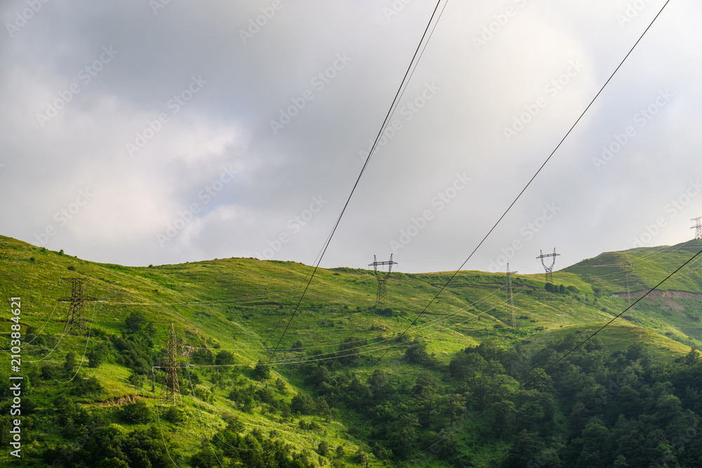 Fototapeta premium Landscape featuring electrical transmission lines over verdant hillsides under o