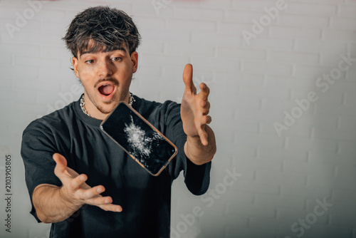 Tableau sur toile A startled young man watches as a cracked smartphone accidentally falls, reactin