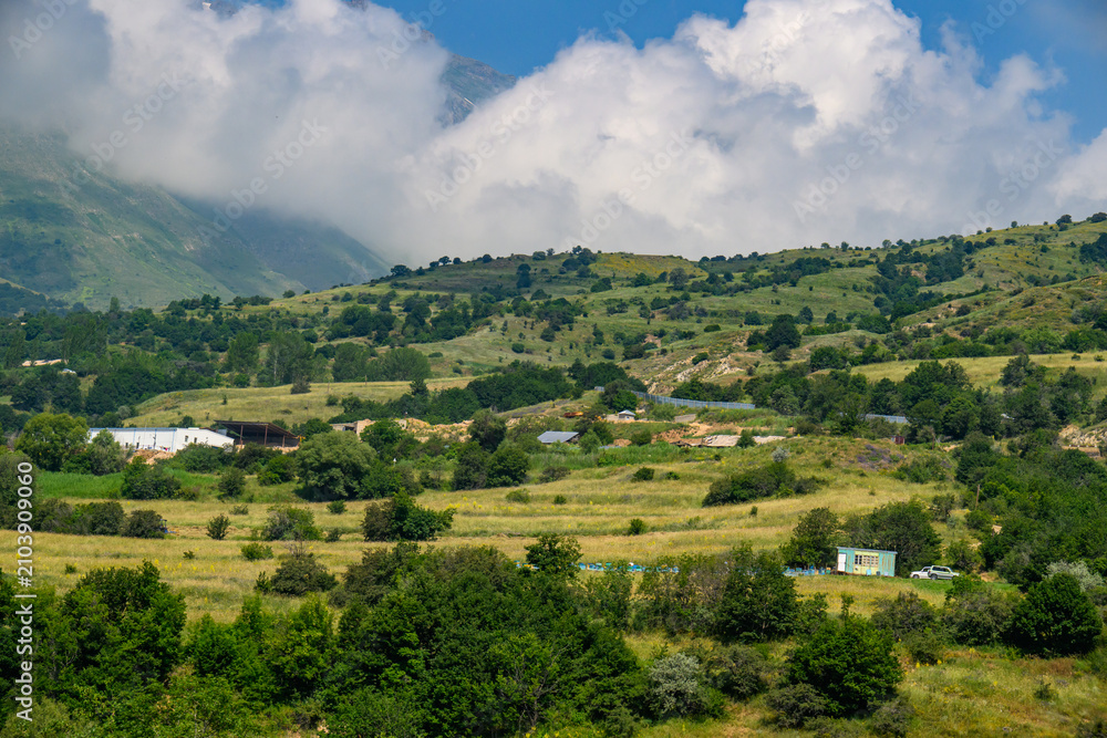Fototapeta premium Mountain valley landscape with clouds, green slopes, and small farmhouses