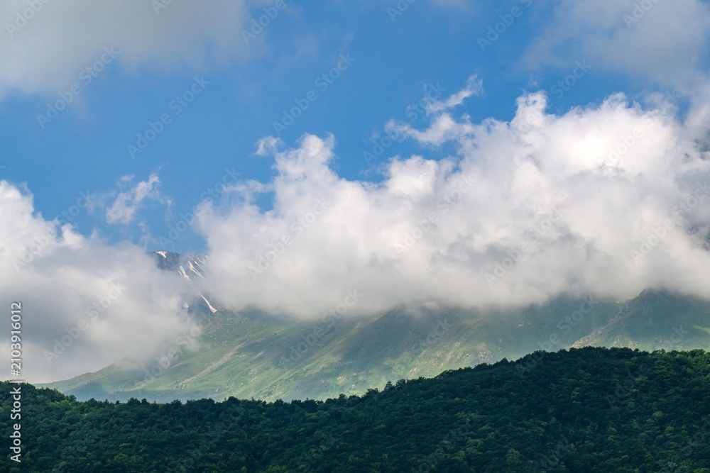 Fototapeta premium Clouds drift over forested mountain ridges under bright blue sky