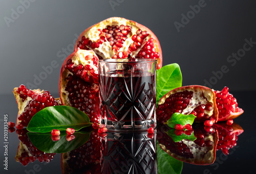 Pomegranate and a glass of ruby-red juice on a black reflective background.