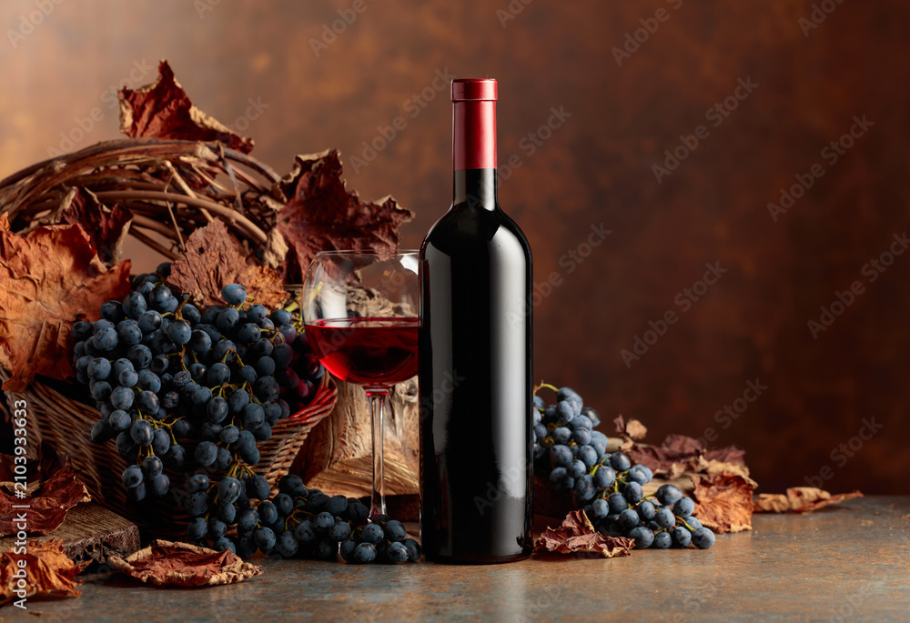 Fototapeta premium Bottle of red wine with blue grapes on a brown background.