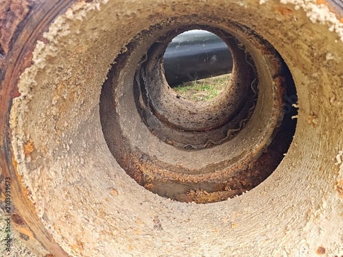 Inside view of a heavily corroded industrial water pipe showing severe limescale, calcium mineral deposits, and rust buildup