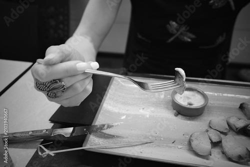 Woman holding roasted potato with fork during restaurant meal in black and white