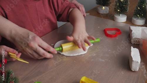 Toddler playing with air dry clay and making handmade holiday decorations at home. Three-year-old boy shaping air dry clay with toy tools at home. Cozy holiday atmosphere with miniature Christmas tree