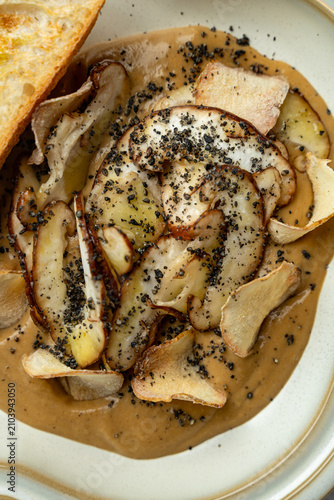 A plate shows different kinds of mushrooms with a brown sauce. Bread sits on the side. The scene occurs in a restaurant during lunch time