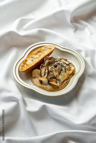 A plate holds a serving of food with pasta shaped like small pillows covered in a creamy sauce. A piece of bread sits beside the dish on a white cloth