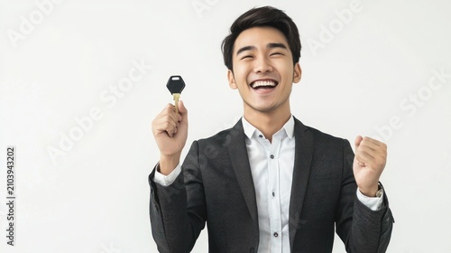 A smiling man in a black suit holds a key above his head, celebrating joyfully against a plain white background.