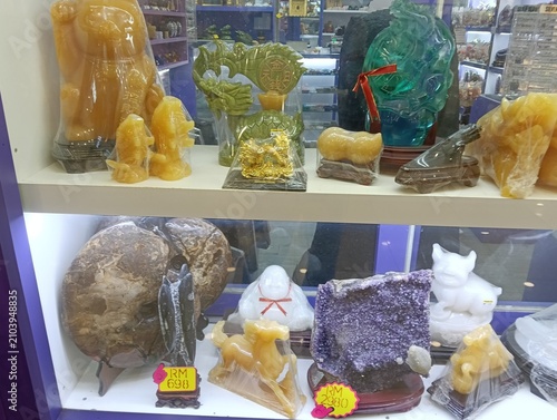 A retail display case showcasing a variety of decorative gemstone and crystal carvings, including translucent jade-like sculptures, white stone animal figurines, Buddha statues, crystal ornaments, and