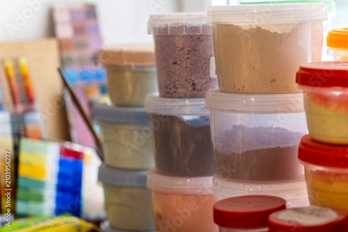 Photography Plastic containers filled with colorful glass enamel powders and artist pigments stand on a workbench in a creative workshop, close up view with selective focus