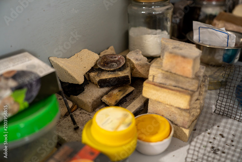 Fotografía Refractory firebricks, broken chamotte block pieces, and small metal dish on a cluttered workshop table used for insulation and heat resistant support in enamel firing