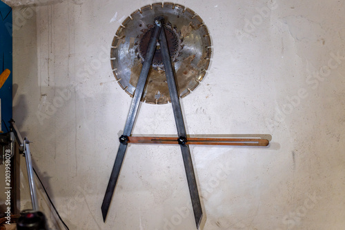 Tableau sur toile Large metal proportional divider caliper tool and circular saw blades hanging on a concrete wall inside a workshop or industrial manufacturing studio
