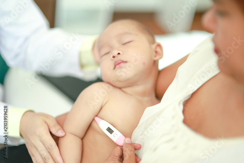 Photography Female doctor gently used digital thermometer measure the body temperature sleeping baby boy in his mother's warm arms inside the clinic demonstrating the attentiveness safety and care medical team