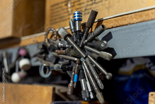 Metal rotary burrs, drill bits, and screwdriver attachments fixed on a round magnetic holder attached to a shelf in a workshop workspace.