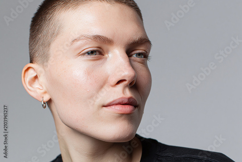 Young adult with short hair clean skin natural makeup hoop earring neutral background close up portrait confident expression